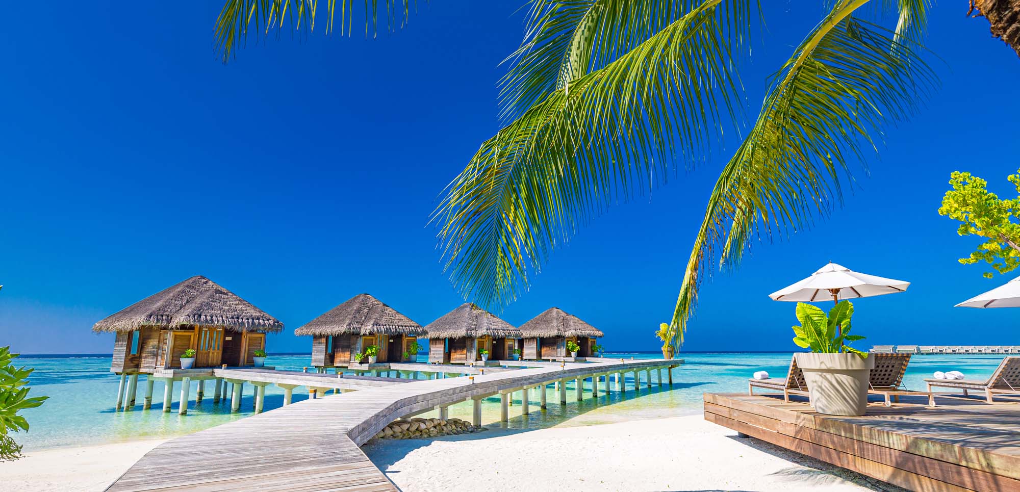 Tropical beach resort with overwater bungalows, white sand, and turquoise lagoon under clear blue sky