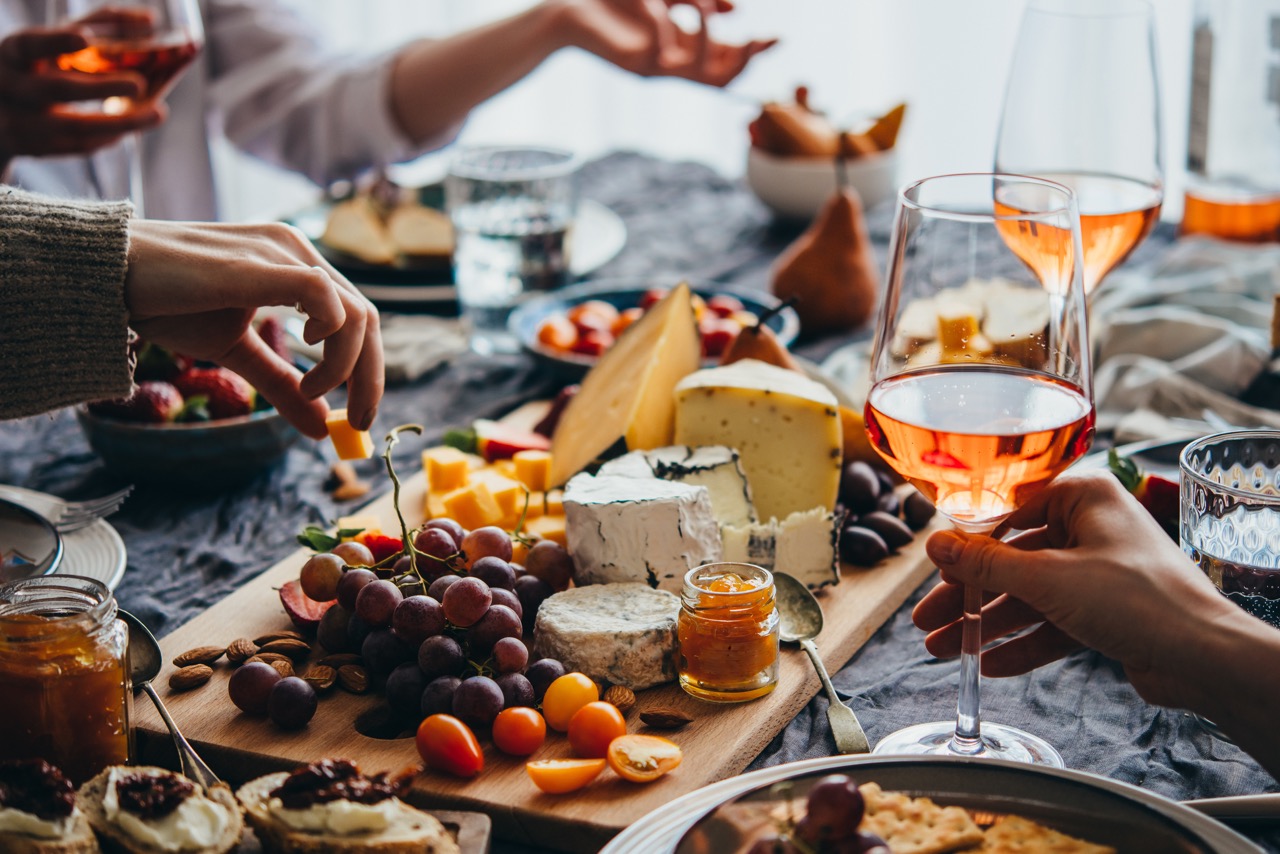 Dinner party Hands reaching for cheese and grapes at a wooden board with wine glasses and charcuterie spread